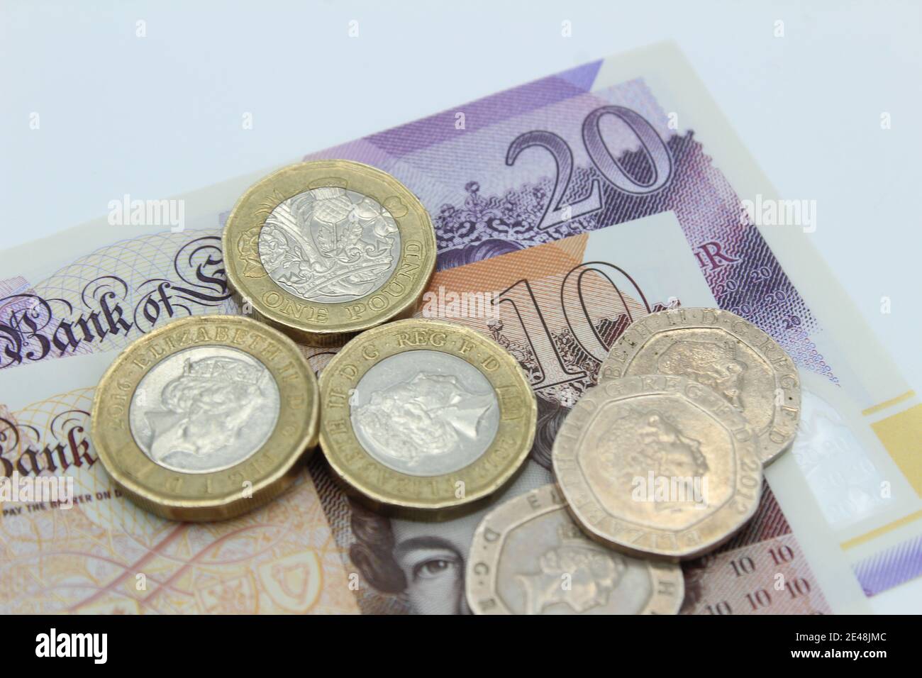 Valuta britannica in sterline di banconote e monete da dieci e venti sterline su sfondo semplice Foto Stock