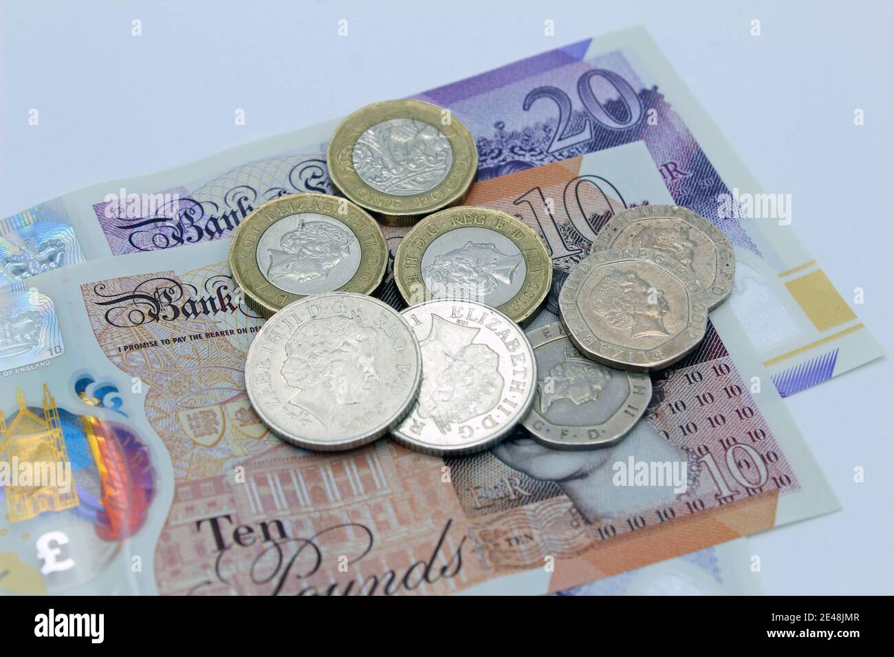 Valuta britannica in sterline di banconote e monete da dieci e venti sterline su sfondo semplice Foto Stock