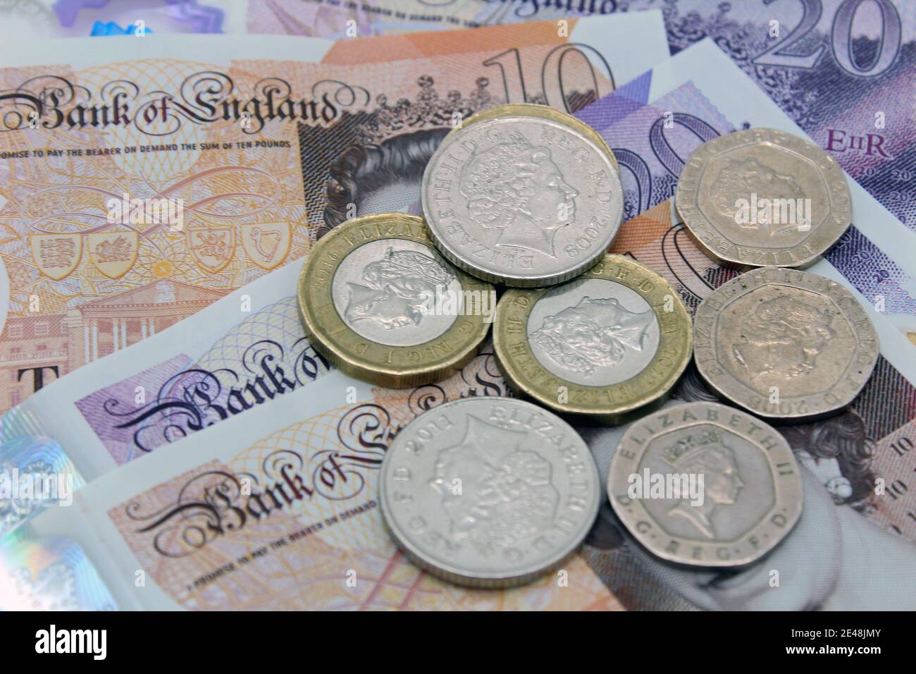Valuta britannica in sterline di banconote e monete da dieci e venti sterline su sfondo semplice Foto Stock