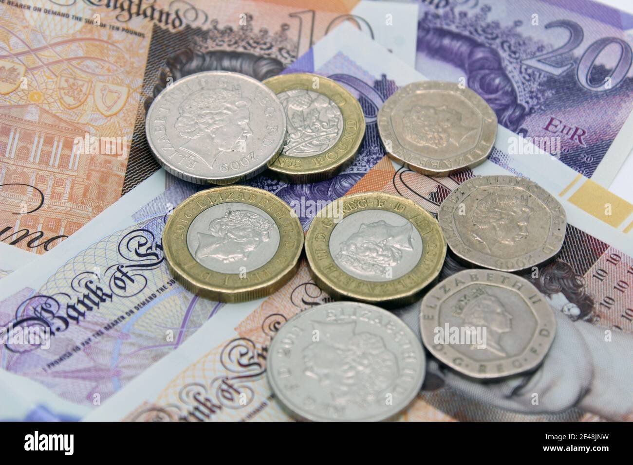 Valuta britannica in sterline di banconote e monete da dieci e venti sterline su sfondo semplice Foto Stock