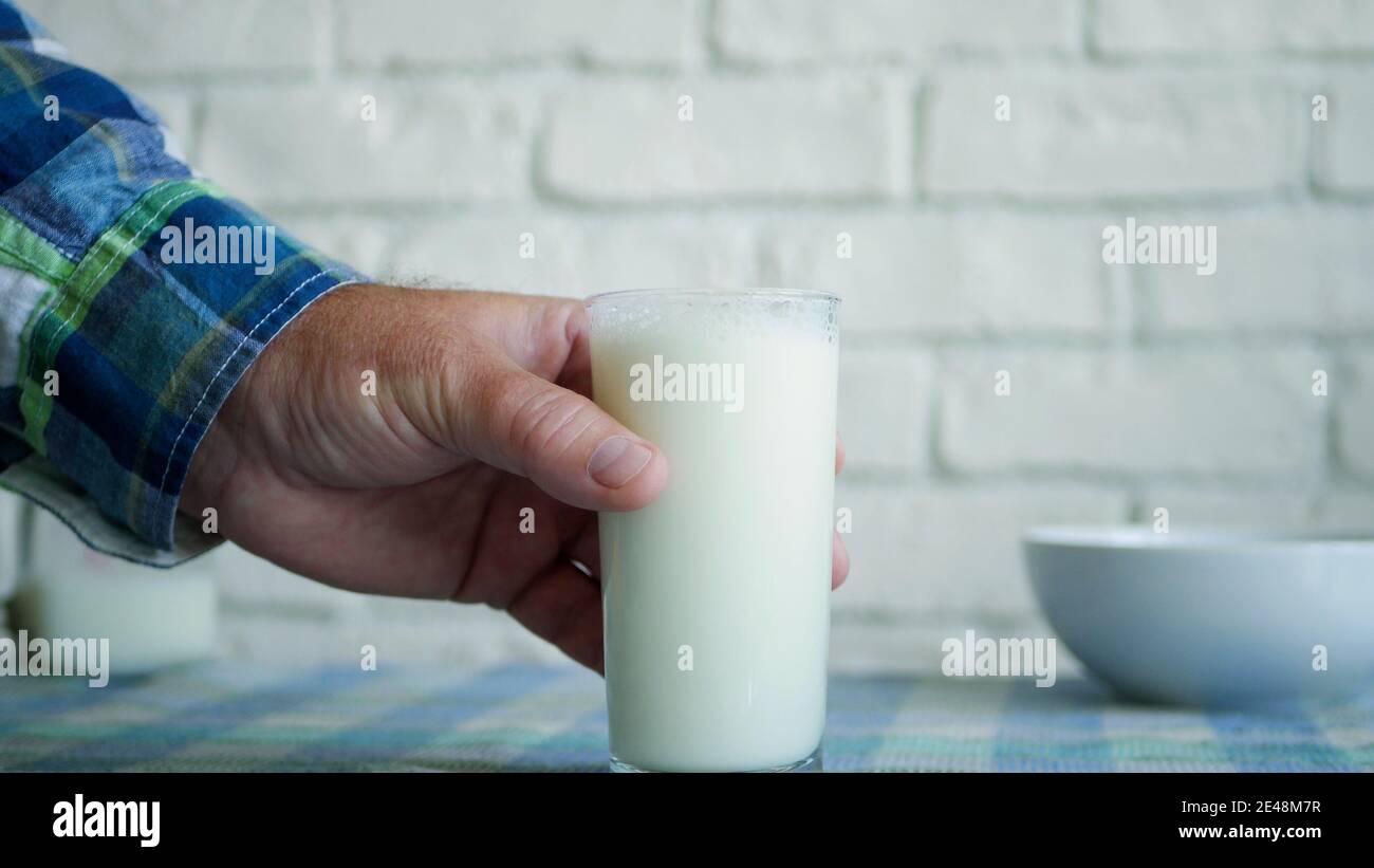 Una persona prende e beve un bicchiere con latte fresco a colazione una bevanda sana, gustosa e naturale piena di proteine e vitamine Foto Stock