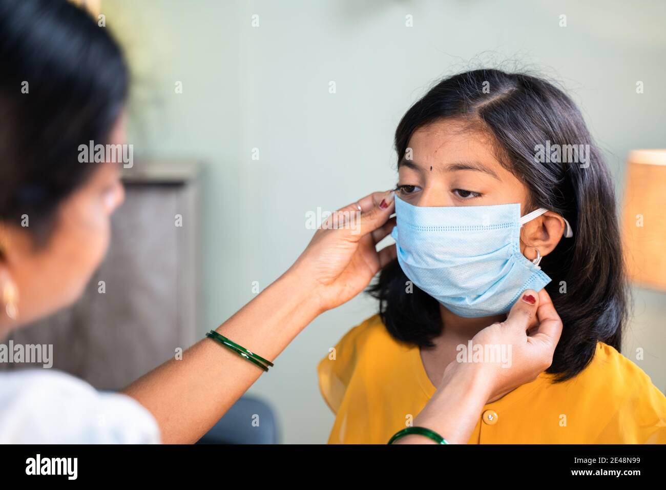 Madre che aiuta la figlia a indossare la maschera facciale prima di andare a scuola a casa come coronavirus covid-19 misure di sicurezza sanitaria - concetto di ritorno a s. Foto Stock