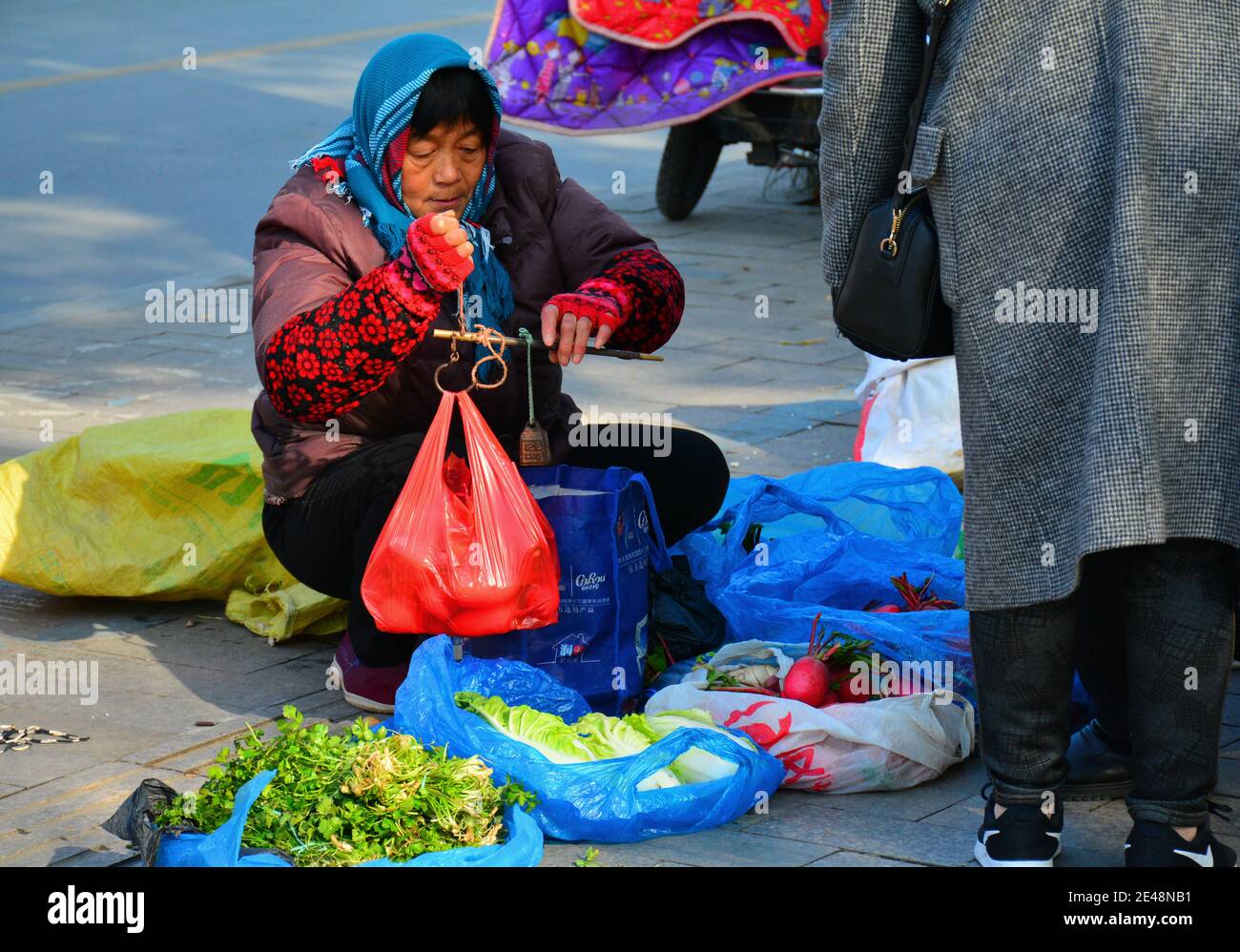 Donna che vende frutta e verdura per strada, utilizzando scale molto vecchio stile per pesare gli oggetti. Foto Stock