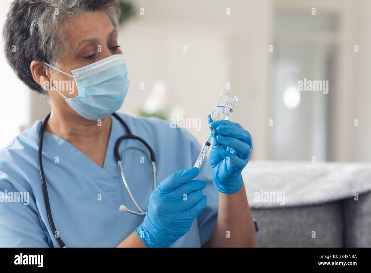 Senior african american femmina medico indossando maschera viso preparazione della vaccinazione a casa Foto Stock