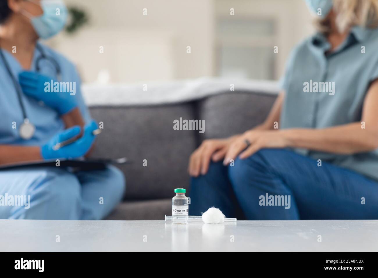 Senior african american medico femminile parlando con paziente femminile entrambi indossare maschere a casa Foto Stock