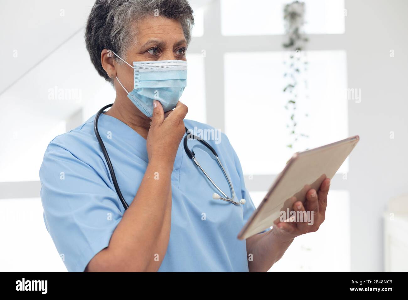 Senior african american medico femminile indossando una maschera viso utilizzando un tablet digitale Foto Stock