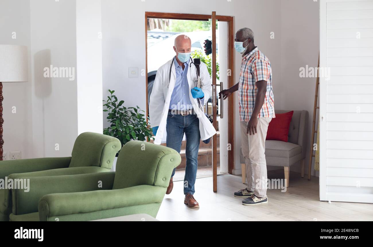 Alto africano americano uomo saluto caucasico senior medico entrambi indossando maschere a casa Foto Stock