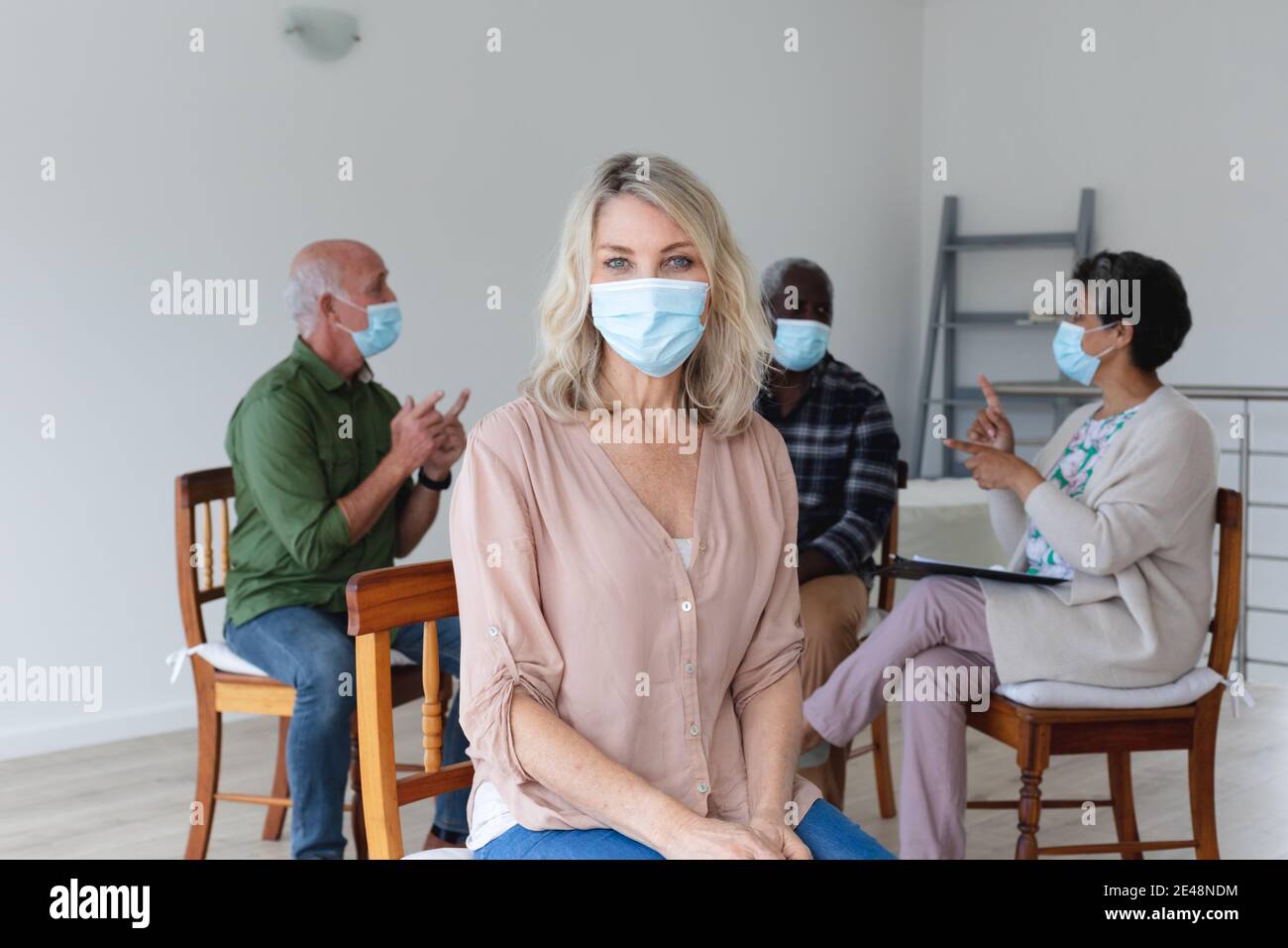 Gruppo vario di anziani che indossano maschere di faccia che parlano durante un sessione di terapia di gruppo a casa Foto Stock