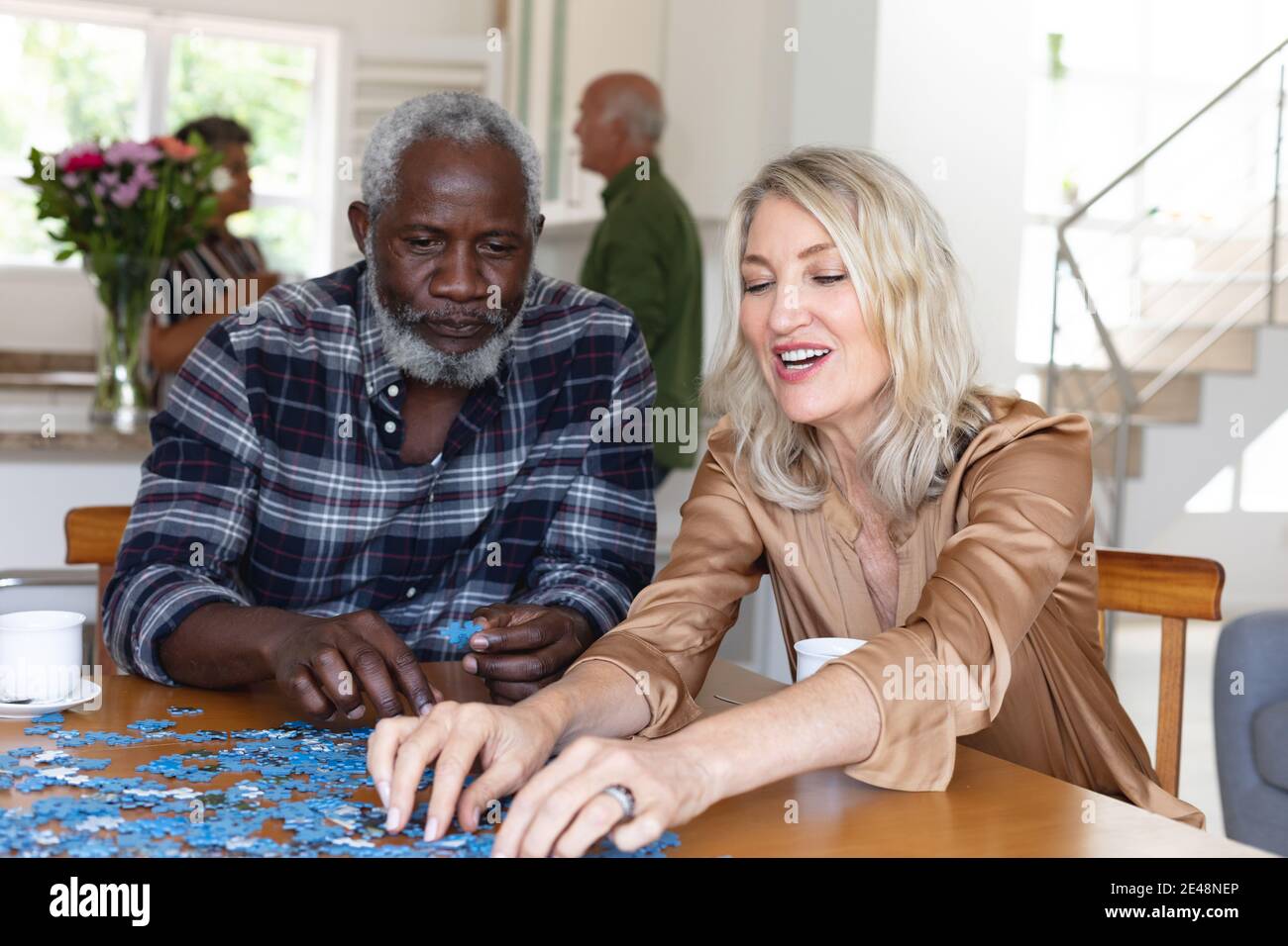 Donna caucasica anziana e uomo afroamericano seduto al tavolo fare puzzle a casa Foto Stock