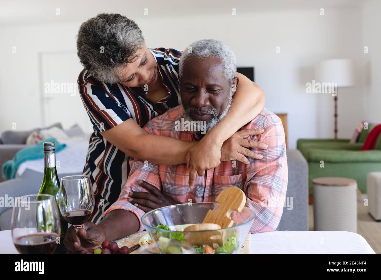 Senior african american coppia seduta al tavolo cena e. abbracciare a casa Foto Stock