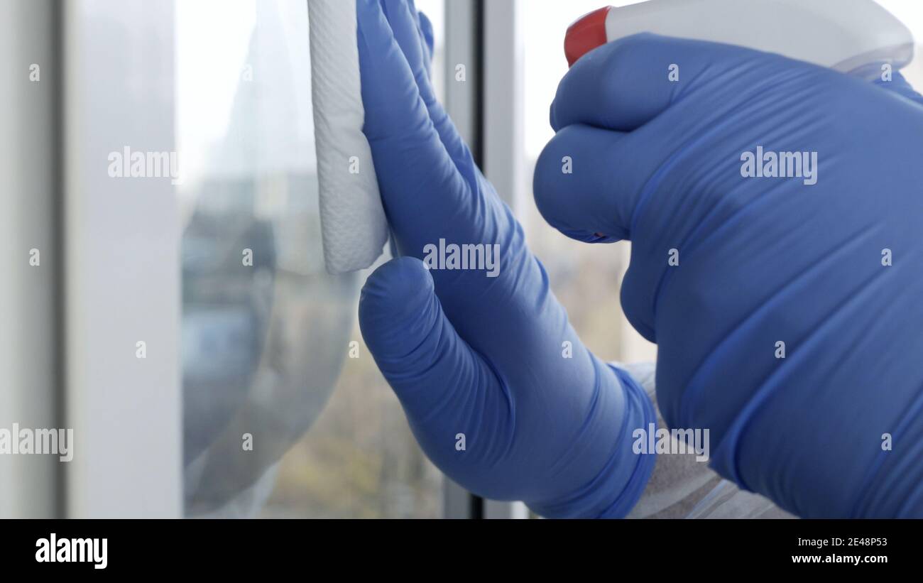 Primo piano mani dell'uomo con guanti di protezione pulizia di una finestra con liquido spruzzato disinfezione contro la contaminazione da virus Foto Stock