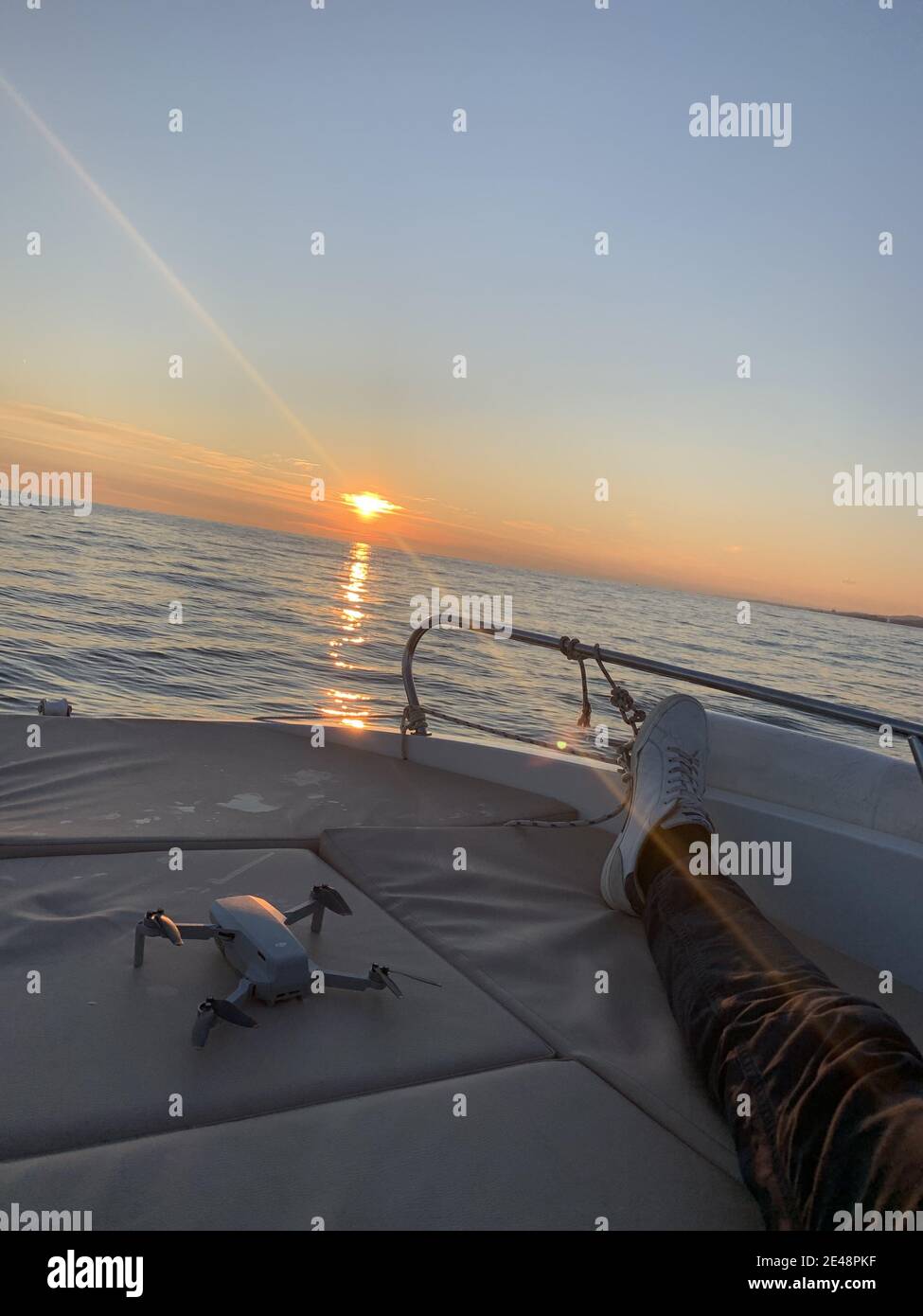 Immagine verticale della gamba di qualcuno che mostra solo e un drone su una barca al tramonto Foto Stock