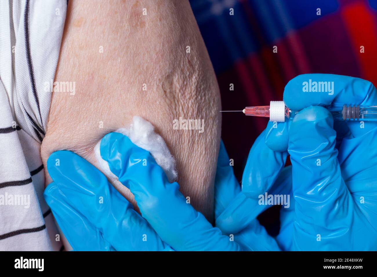 L'uomo molto anziano sta ricevendo il vaccino del coronavirus. Primo piano. Iniezione a persone anziane a casa. Siringa con medici mani in guanti blu. Foto Stock