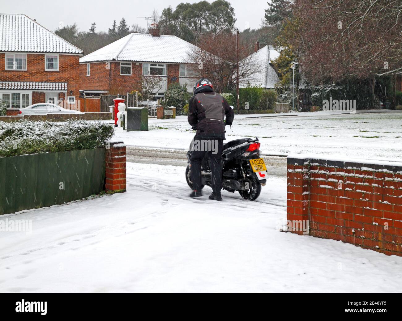 Un motociclista apprendista che spinge la sua moto fuori strada per la sicurezza in condizioni di strada ghiacciata in inverno a Hellesdon, Norfolk, Inghilterra, Regno Unito. Foto Stock