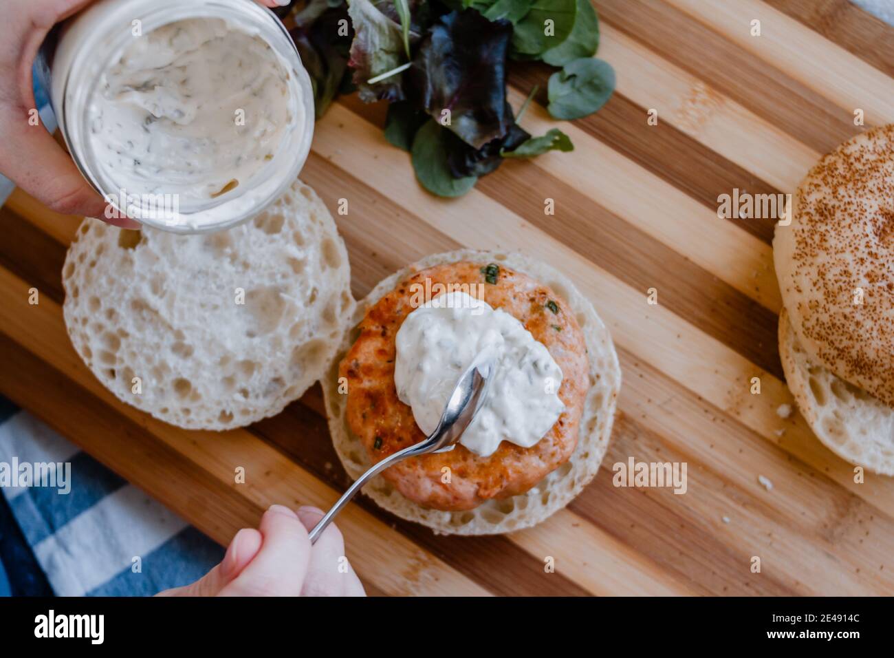 Una donna che saluta la salsa tartara fatta in casa su un salmone e gamberi hamburger Foto Stock