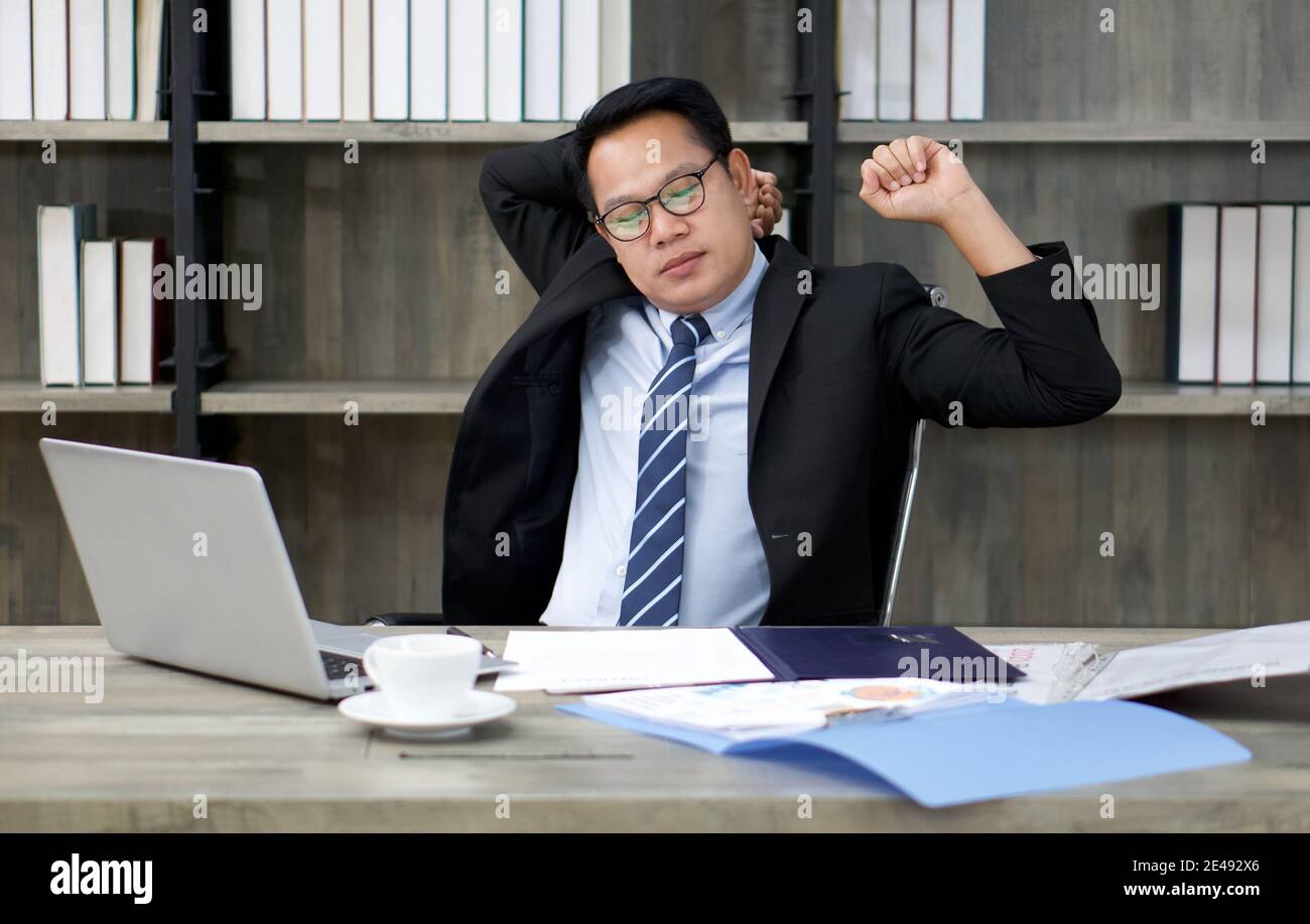 Un uomo d'affari in una tuta si allunga laziosamente mentre si guarda uno schermo del computer. Per alleviare il dolore causato dall'uso prolungato del computer Foto Stock