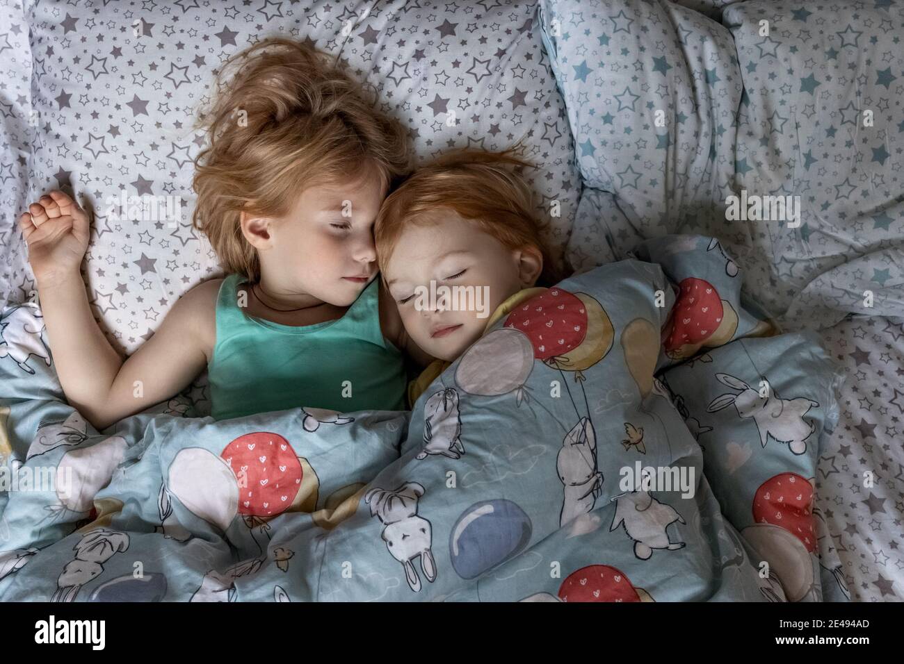 Due piccole sorelle sorelle che dormono in un abbraccio nel letto sotto una coperta. Foto Stock