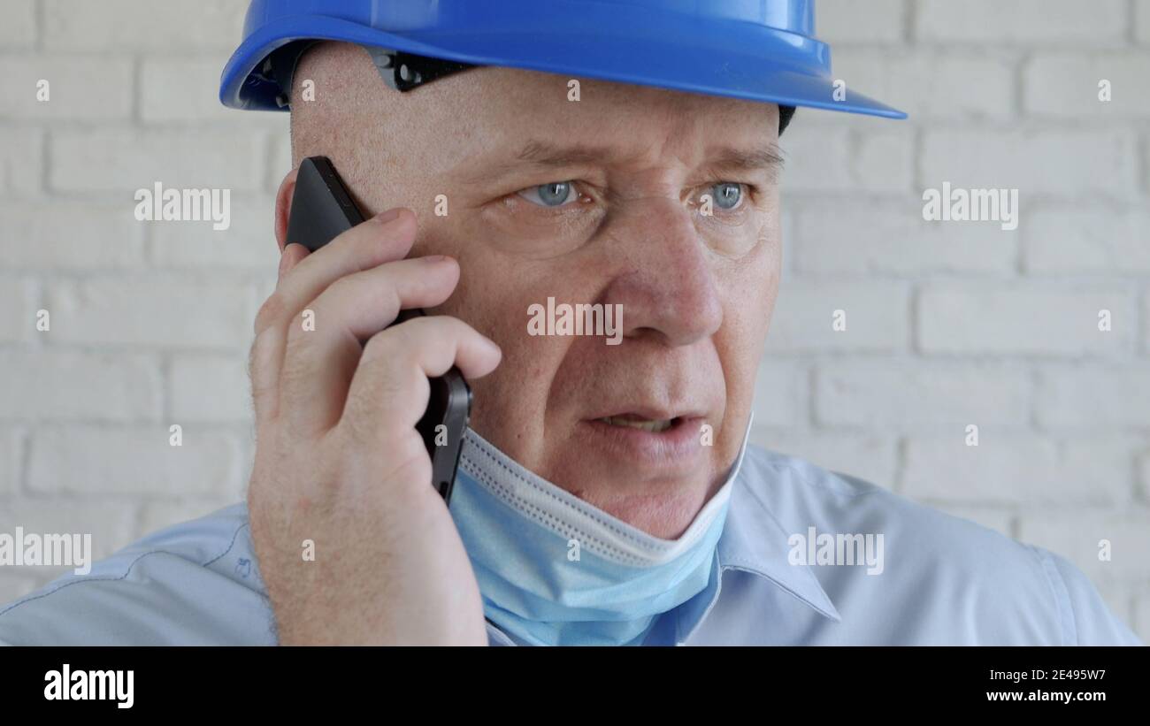 Ingegnere con casco di sicurezza e una maschera di protezione sul viso che parla con il cellulare Foto Stock