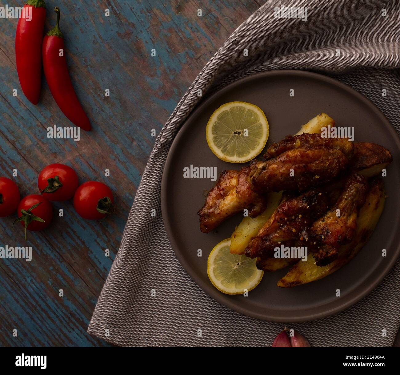 Ali di pollo con miele e spicchi di patate su un piatto con pomodori ciliegini e peperoncini Foto Stock
