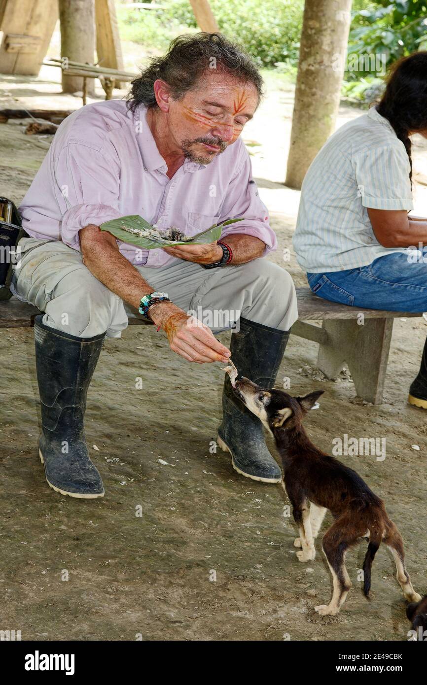 Uomo che alimenta cane, pezzo di pesce, cotto in foglia bagnata, vernice viso, consuetudine locale, Sud America, Amazon Tropical Rainforest, Ecuador Foto Stock