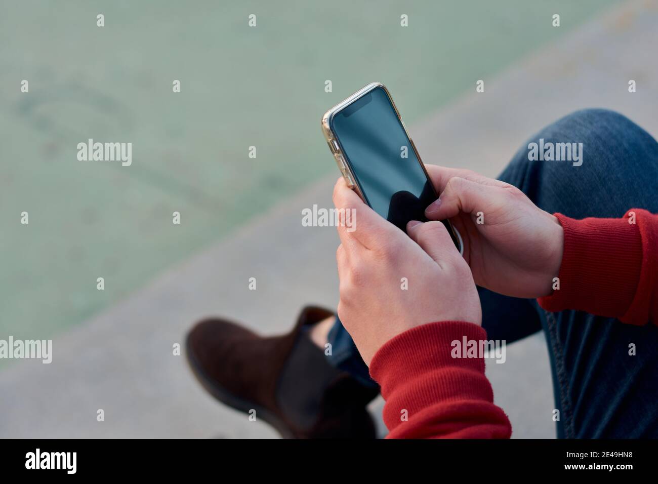 L'uomo studentesco irriconoscibile usa il suo telefono in un campo da basket Foto Stock