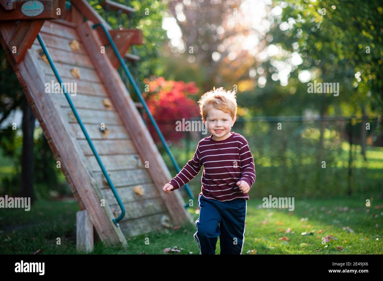 Ragazzo di 3-4 anni che corre attraverso l'erba nel cortile durante l'autunno Foto Stock