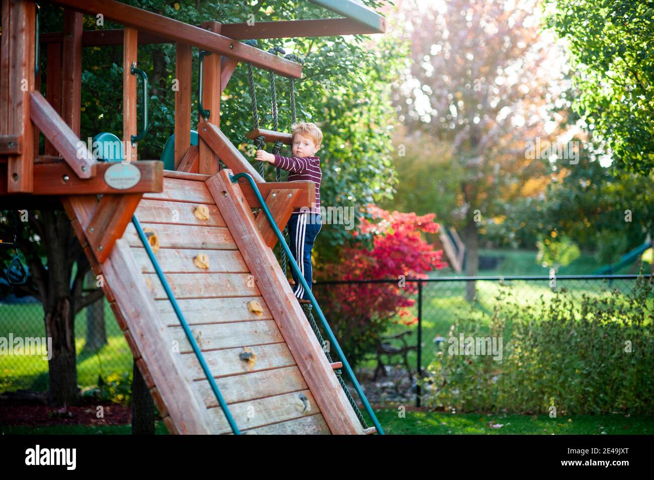 Ragazzo di 3-4 anni sale su scala su swing set In cortile in autunno Foto Stock