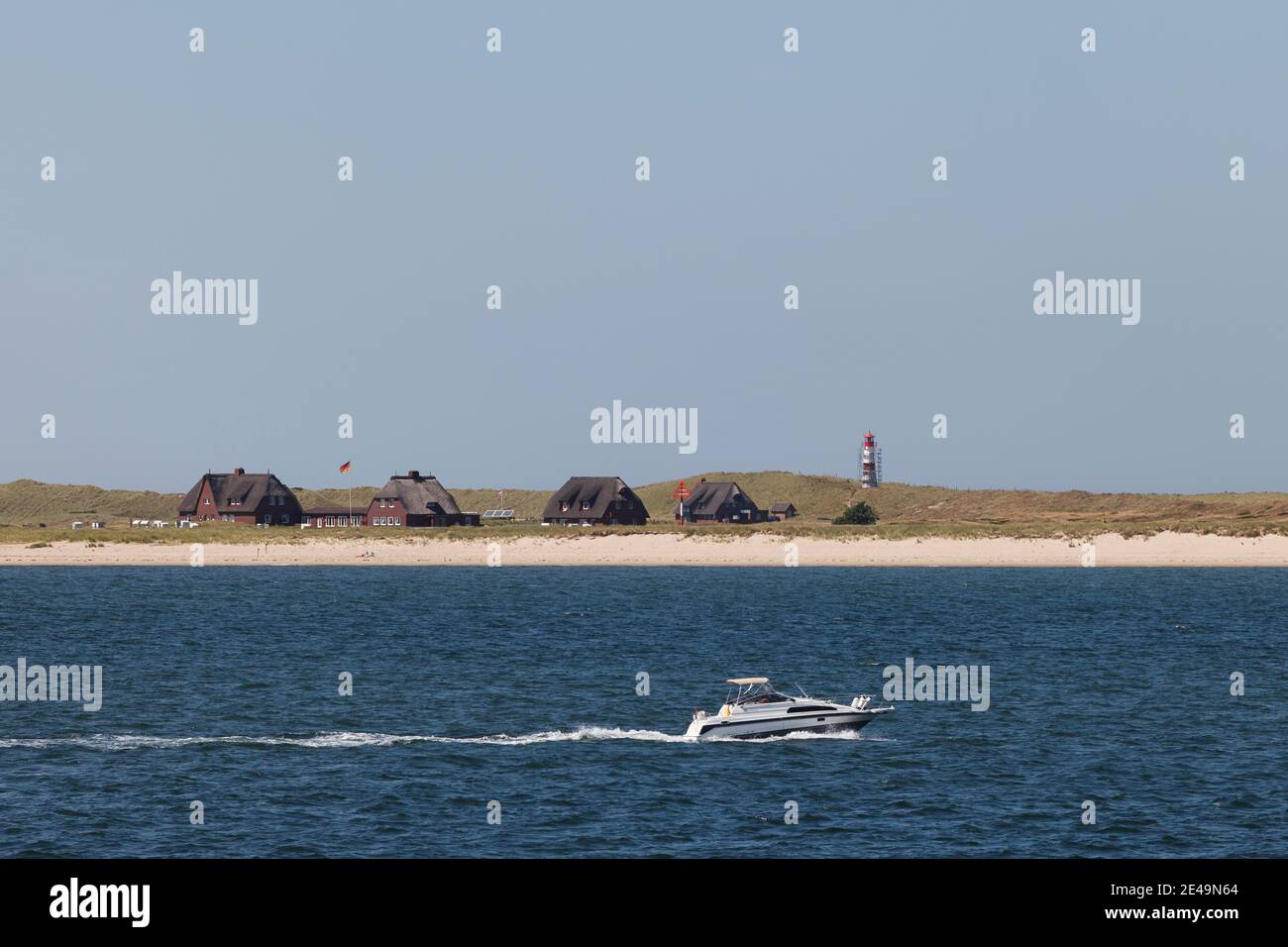 Lo yacht naviga di fronte alle case con tetto di paglia al gomito con una torre faro sullo sfondo sull'isola di Sylt nel Mare del Nord, Frisia del Nord, Schleswig-Holstein, Germania Foto Stock