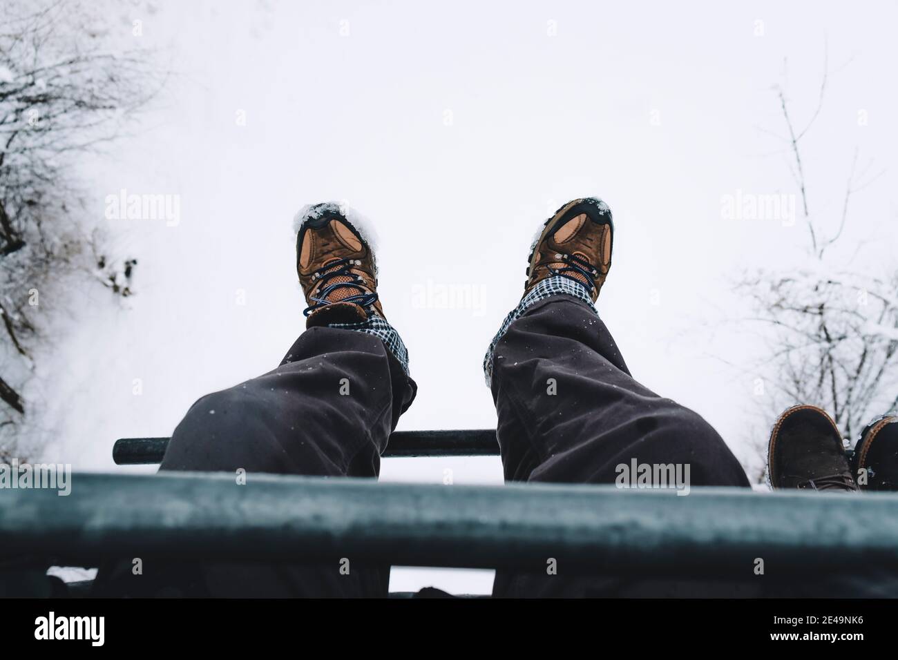 Uomo seduto in skilift con vista aerea, punto di vista, scarpe nell'aria sopra il paesaggio innevato, Foto Stock