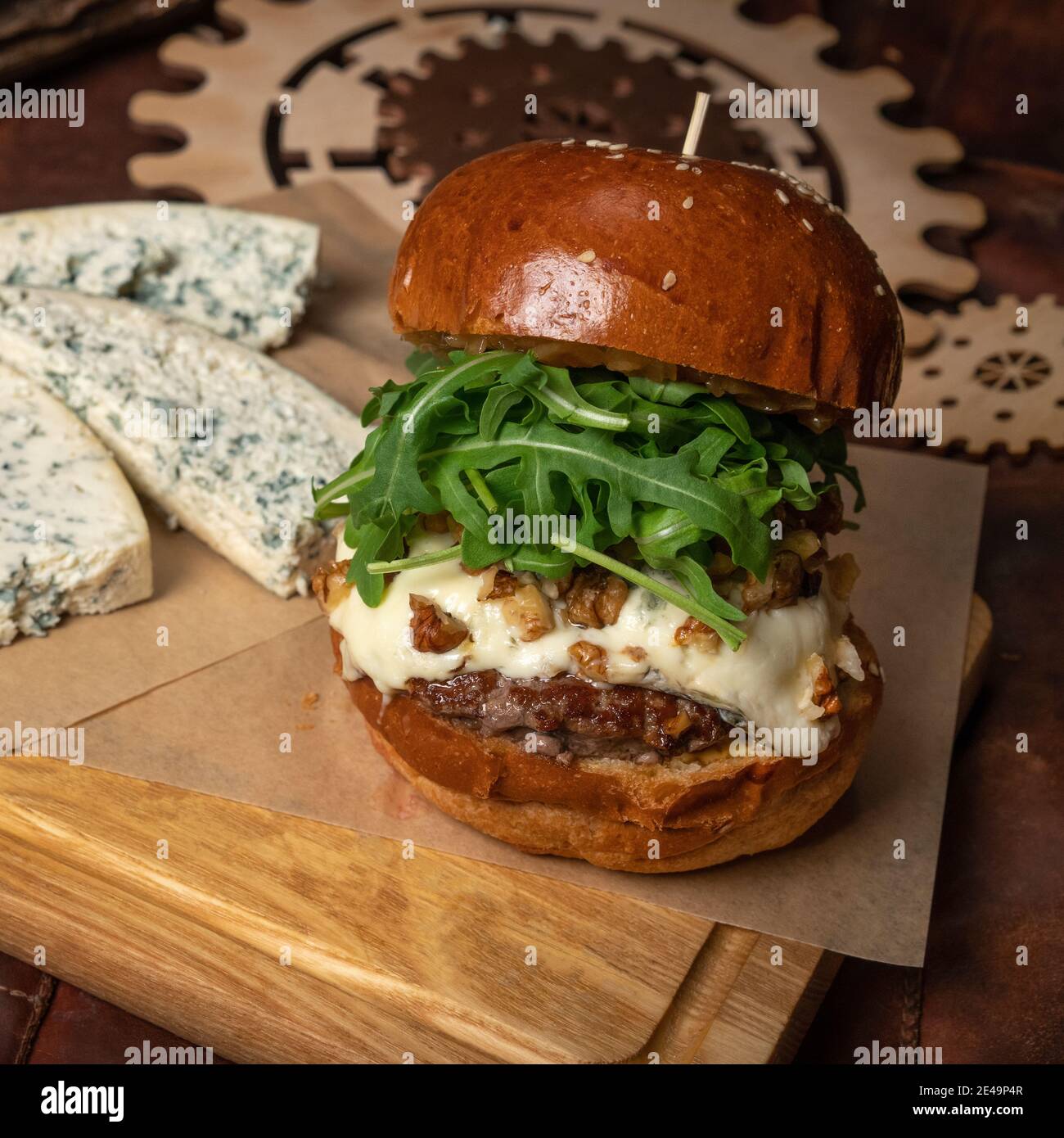 Hamburger di manzo fresco artigianale con insalata di rucola fresca e, fette di formaggio blu fresco adagiato accanto ad esso. Concetto di ristorante. Concetto di Street food Foto Stock