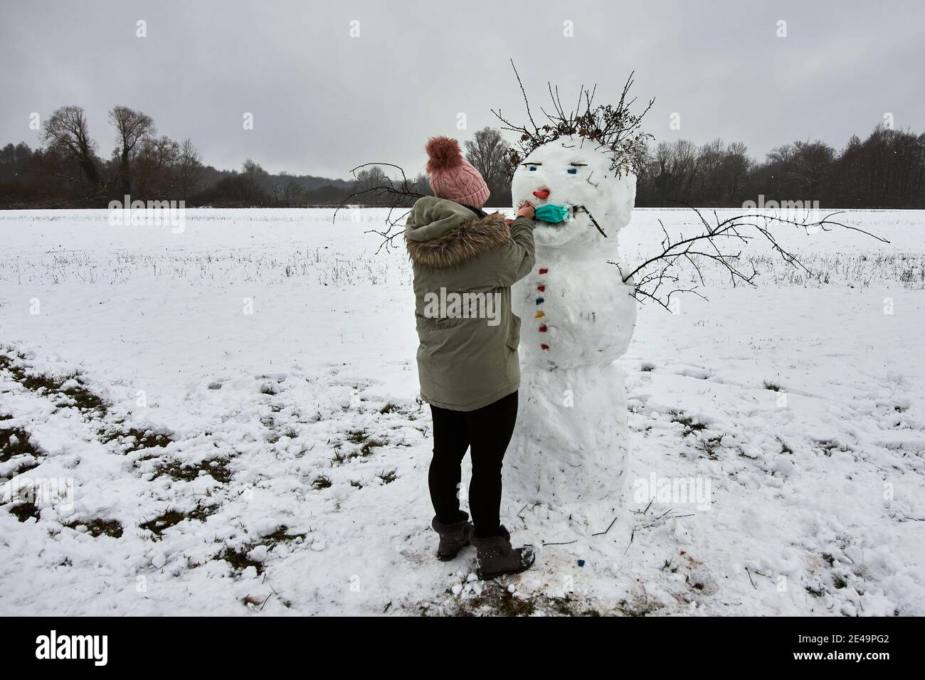 Donna in abiti invernali facendo un simpatico pupazzo di neve aggiungendo medico maschera facciale Foto Stock