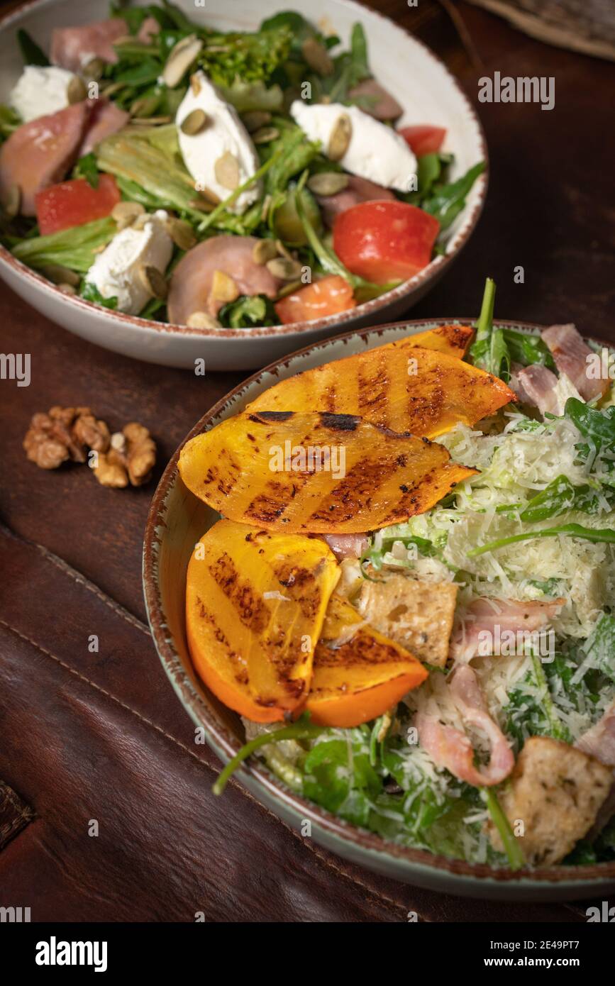 Due ciotole di insalate con salmone, mozzarella e fette di frutta alla griglia si stagliano su un tavolo coperto da uno straccio di cuoio. Concetto di ristorante Foto Stock