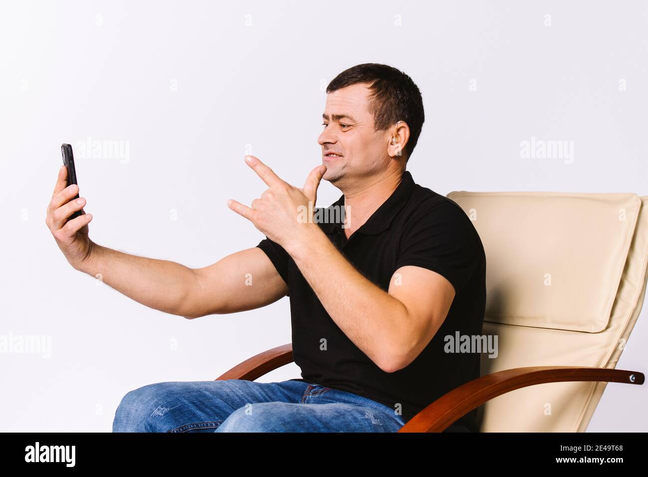 Un uomo seduto in una poltrona di pelle comunica non verbalmente tramite la comunicazione video, mostrando i Love You al suo compagno di soulmate. Sfondo bianco. Foto Stock
