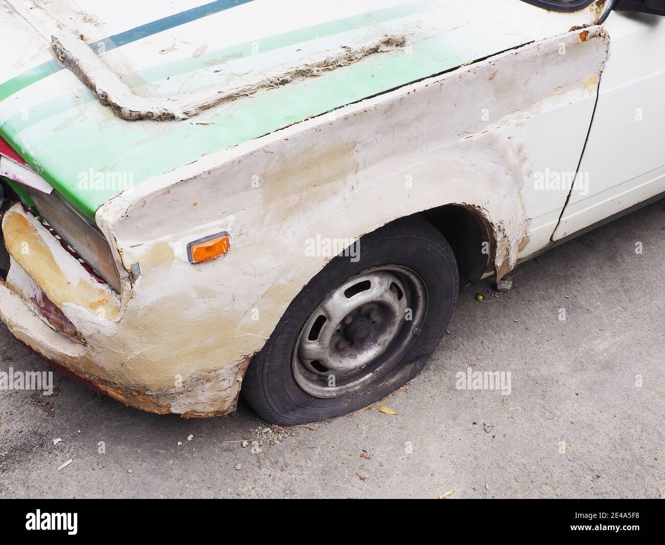 Frammento di una vecchia auto con pneumatico sgonfio, coperto di stucco ruvido Foto Stock