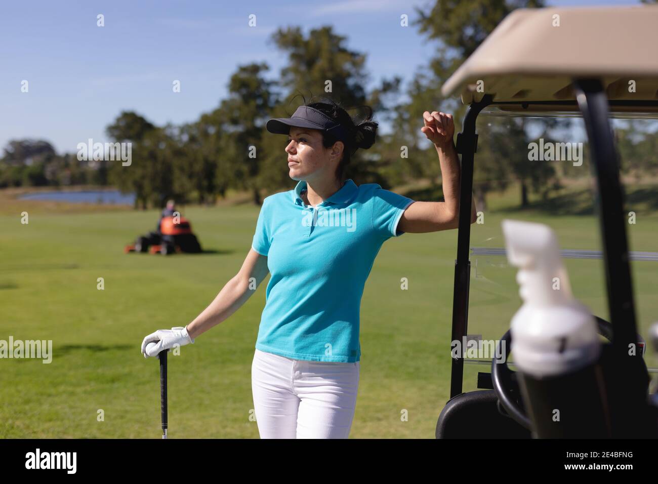 Donna caucasica che gioca a golf appoggiandosi al golf cart corso Foto Stock