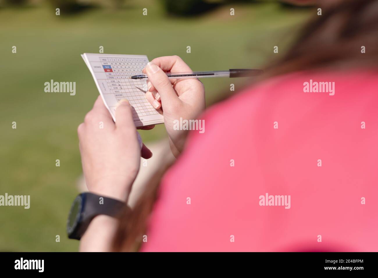 Vista su spalla di donna caucasica che gioca a golf riempiendo scheda di valutazione Foto Stock