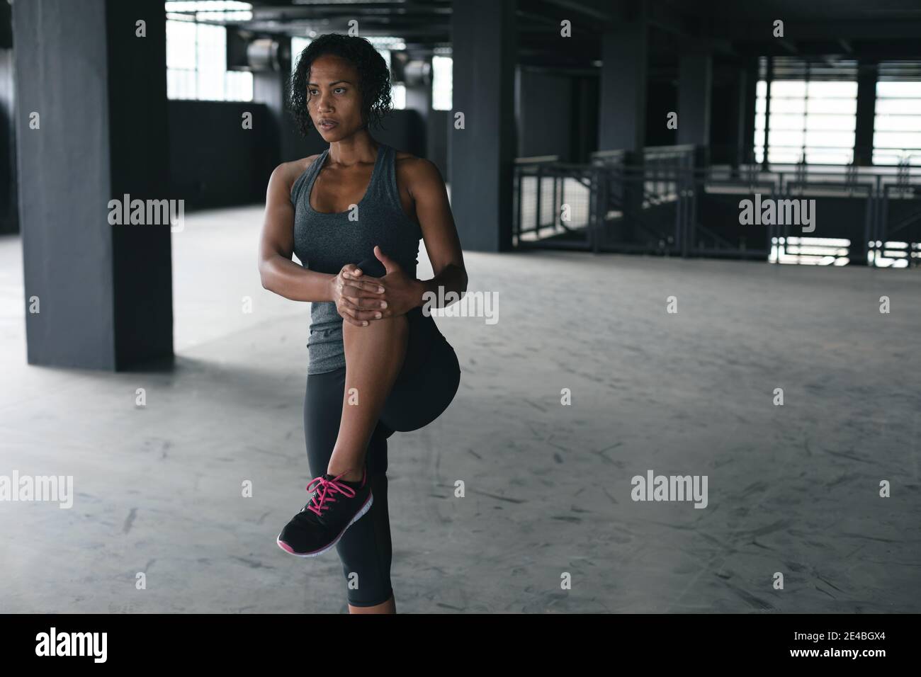 Donna afro-americana in piedi in un edificio urbano vuoto e. stretching Foto Stock