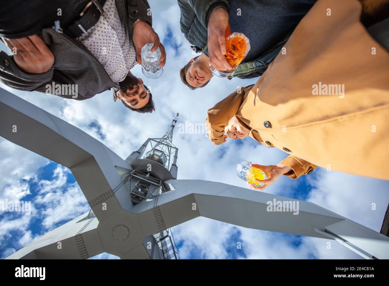 Giovani, tempo libero in città. Tre persone si trovano al porto insieme a un drink in mano. Vista del gruppo dal punto di vista di una rana Foto Stock