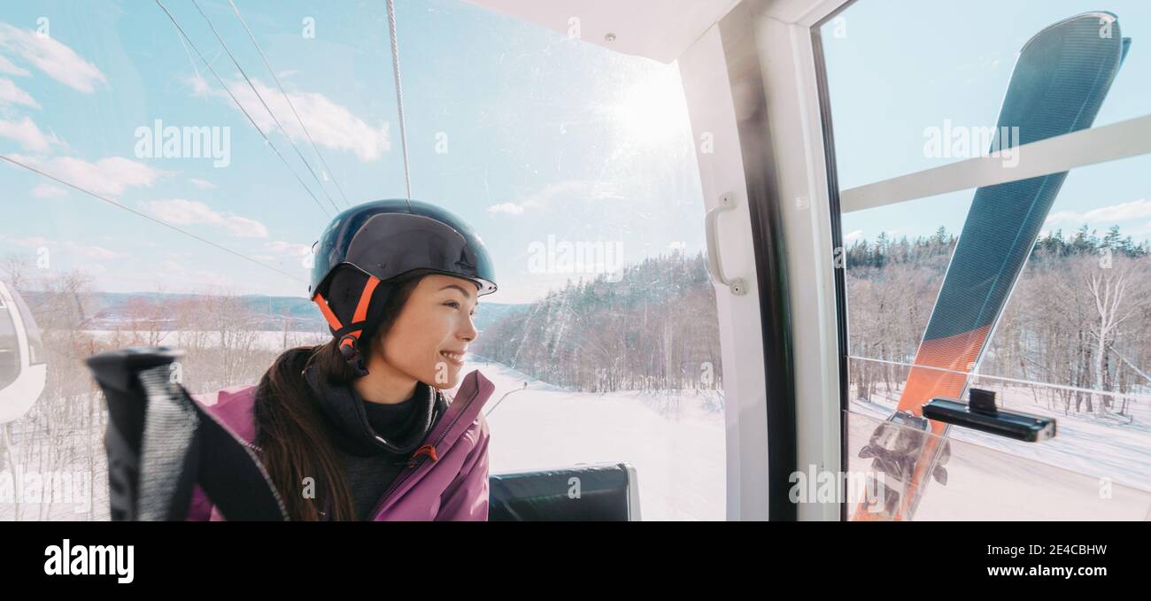 Sport invernale donna asiatica seduta in skilift salendo sulla collina presso la stazione sciistica scendendo le piste. Banner panoramico di sciatore con casco Foto Stock