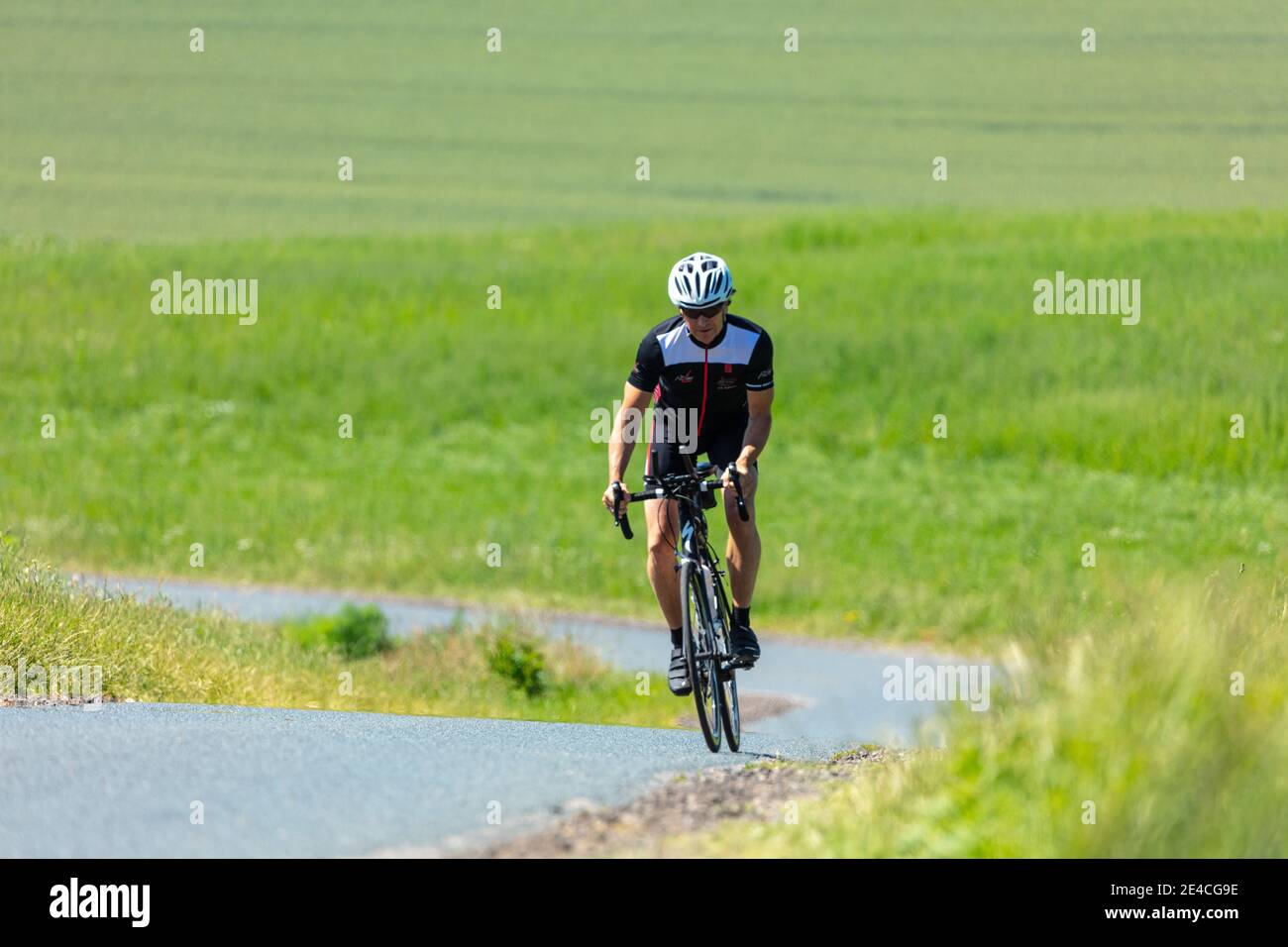 Man 50 Plus, guida la sua bici da corsa attraverso la campagna in estate. Piovendo per il triathlon Foto Stock