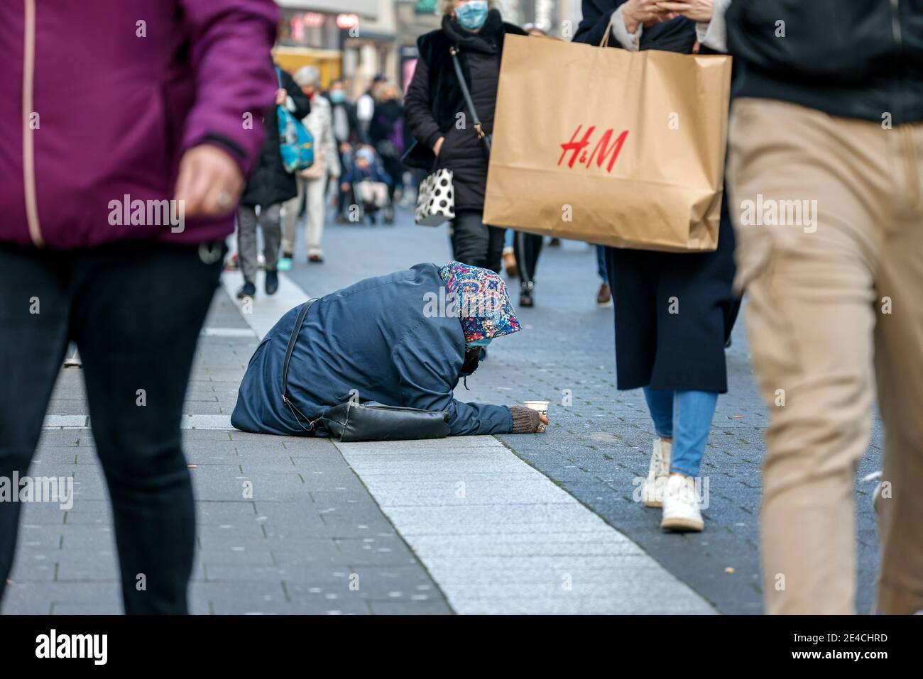 Duesseldorf, Renania Settentrionale-Vestfalia, Germania - UNA donna mendicante si siede sul marciapiede nel centro storico di Duesseldorf in tempi della crisi della corona durante la seconda parte del blocco nel periodo natalizio nella zona pedonale, molti passanti con borse per lo shopping passano oltre. Foto Stock