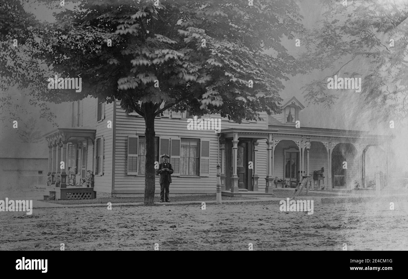 Archivio americano foto monocromatica di un uomo che si trova fuori di una grande casa di ciottoli con portici. Preso nel tardo 19 ° secolo a Port Byron, New York, Stati Uniti Foto Stock