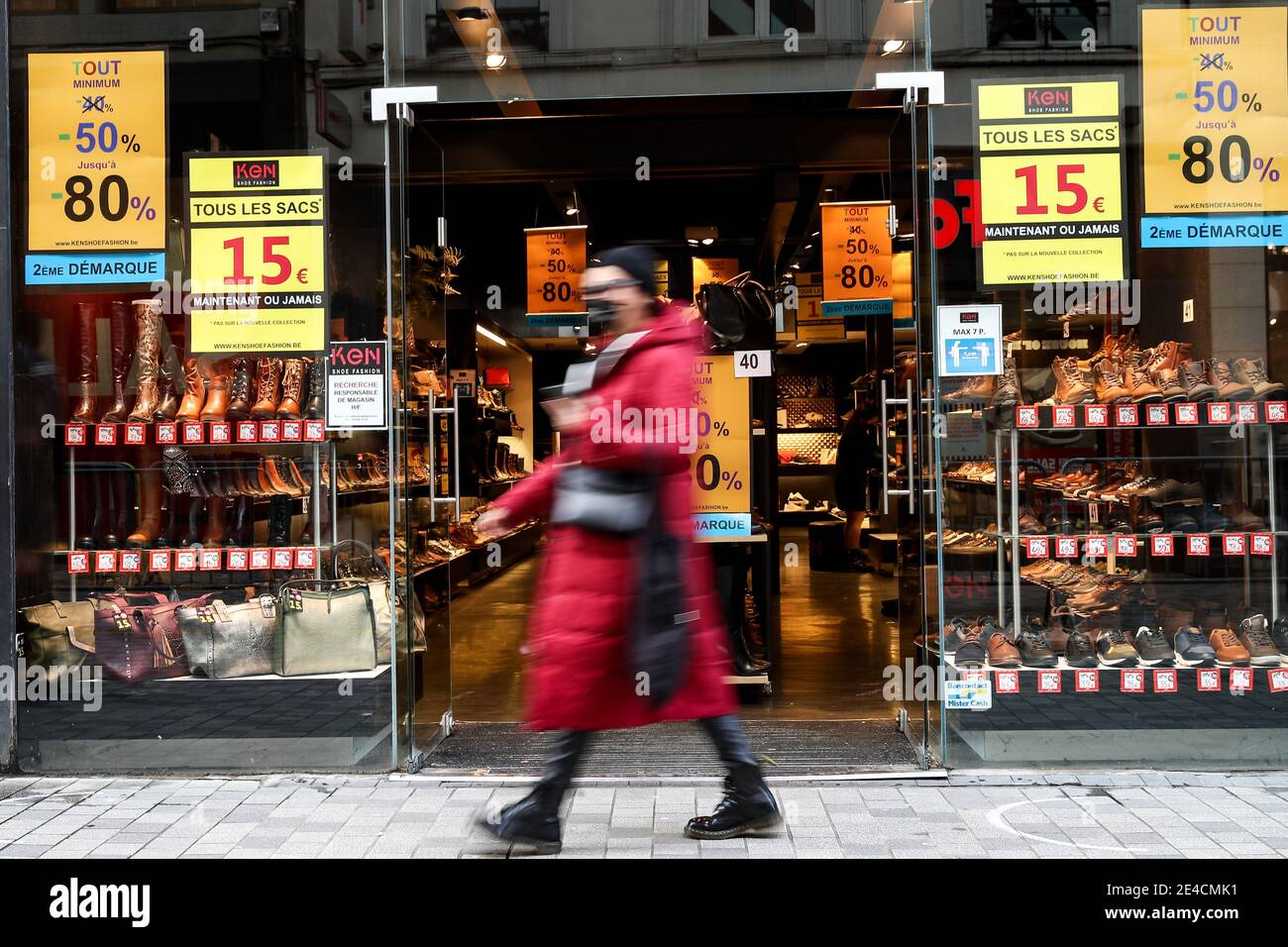 Bruxelles, Belgio. 22 gennaio 2021. Una donna che indossa una maschera passa davanti a un negozio con poster di vendita a Bruxelles, Belgio, 22 gennaio 2021. Le vendite invernali belghe sono nate il 4 gennaio. Per aumentare il consumo, le vendite invernali previste per quattro settimane sono state prorogate di due settimane fino al 15 febbraio. Credit: Zhang Cheng/Xinhua/Alamy Live News Foto Stock