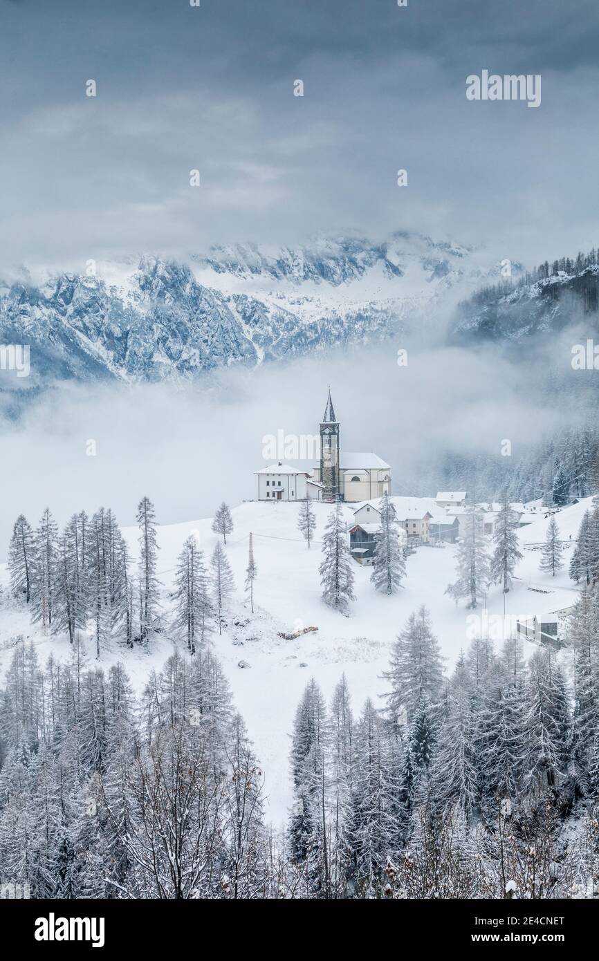 Italia, Veneto, provincia di Belluno, Rocca Pietore, Agordino, il paese di Laste in inverno con la chiesa di San Gottardo sulla collina, Dolomiti Foto Stock