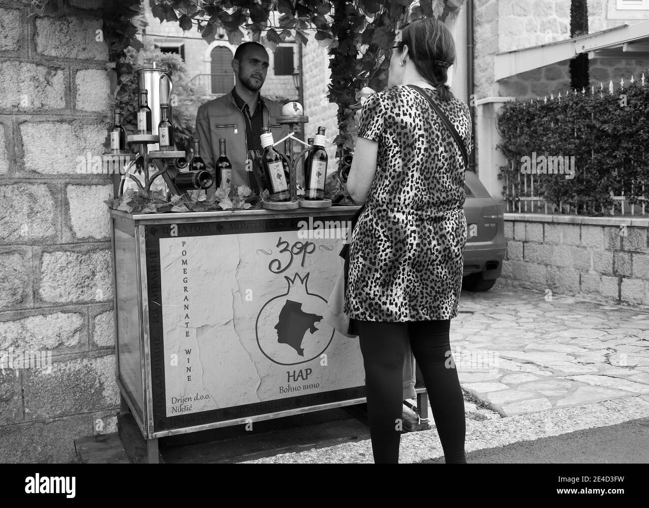 Montenegro, 3 maggio 2019: Turistica femminile che mostra interesse per il vino di melograno domestico che promuove su una bancarella di strada a Perast (B/W) Foto Stock