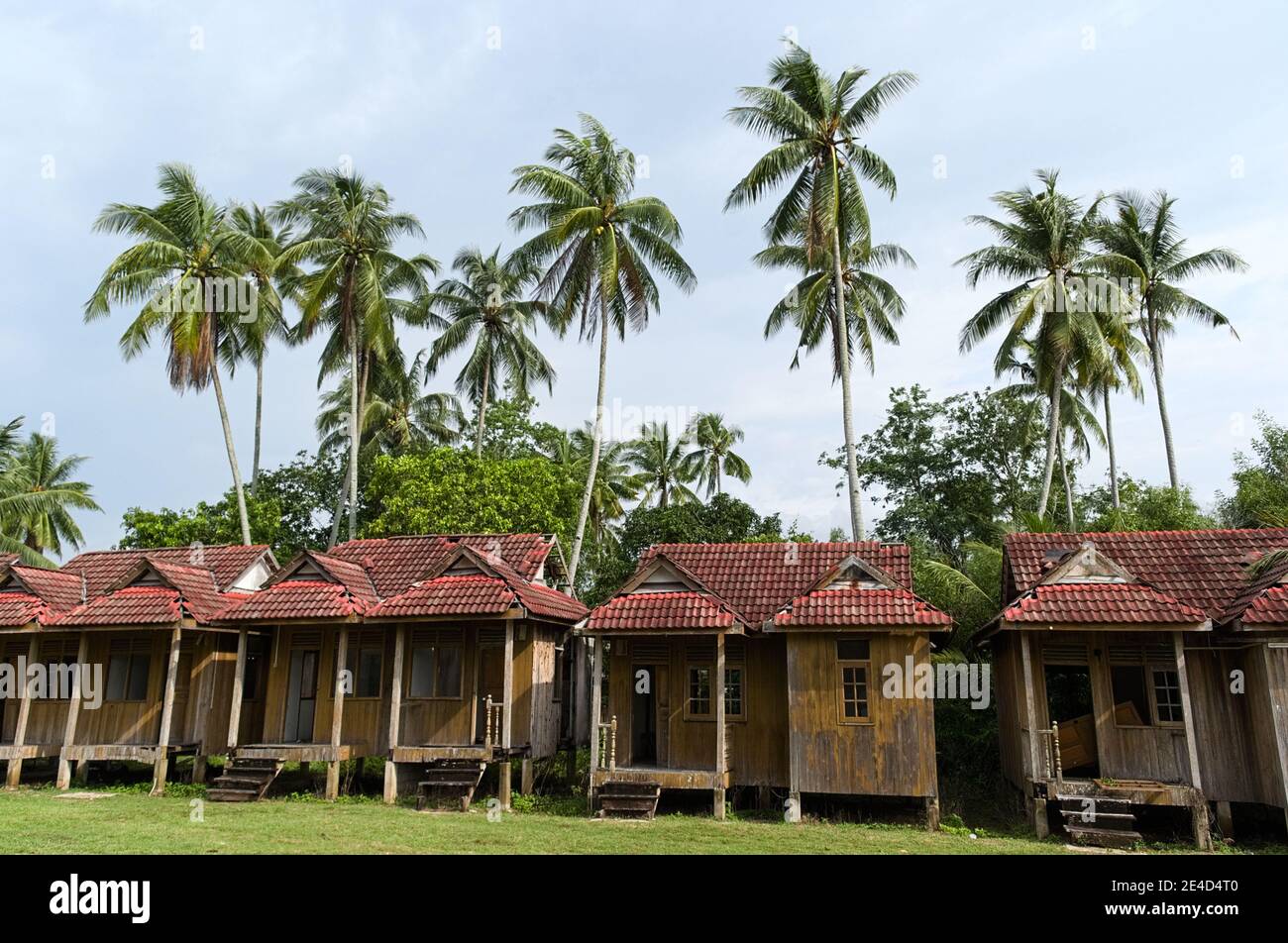 Piccoli bungalow vicino a palme. Capanne in legno intemperie in tradizionale paesaggio tropicale. Scena rurale in piccolo villaggio. Kampung Merang, Malesia Foto Stock