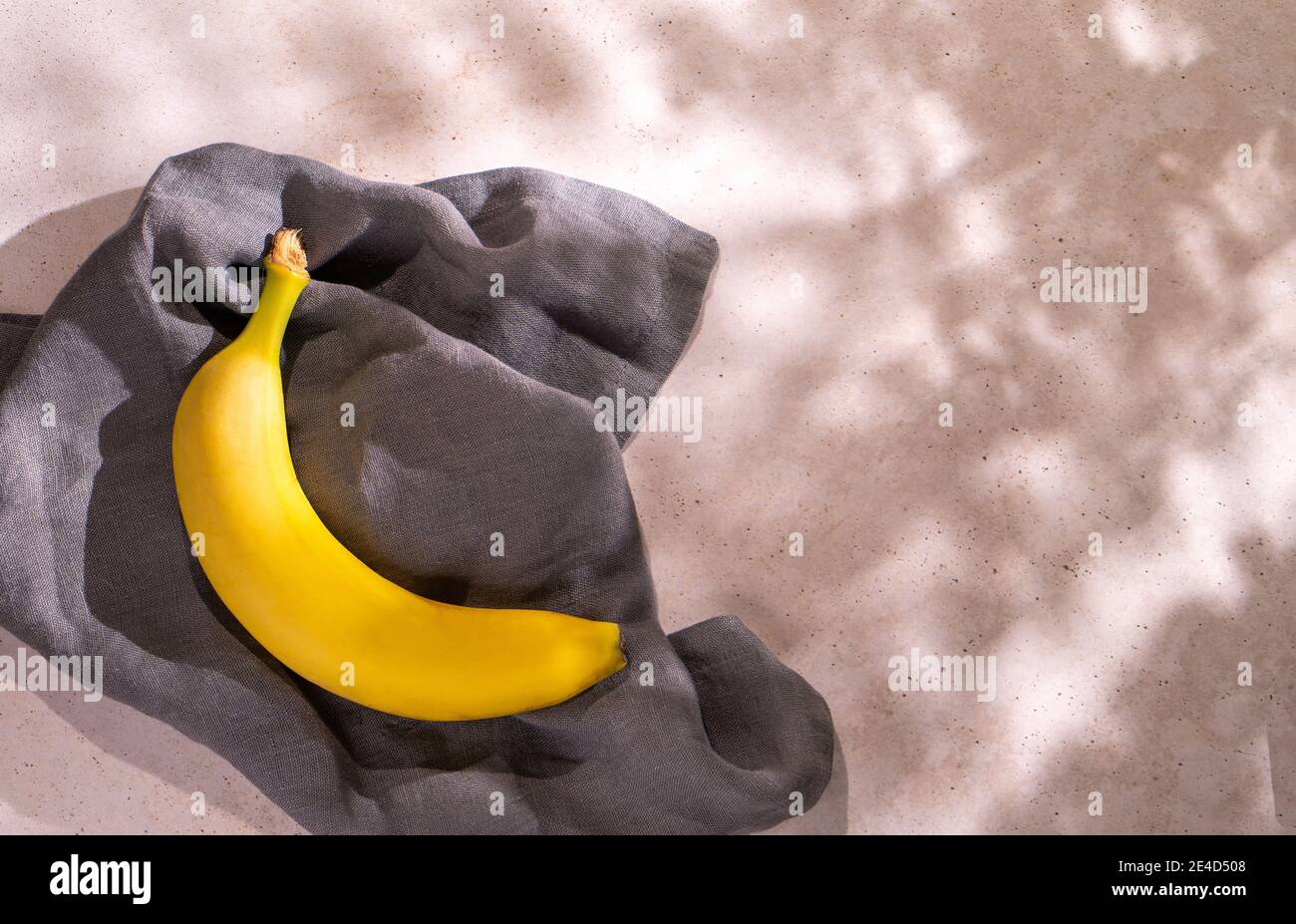 Una banana gialla fresca adagiata su un tovagliolo grigio una superficie in calcestruzzo con spazio di copia Foto Stock