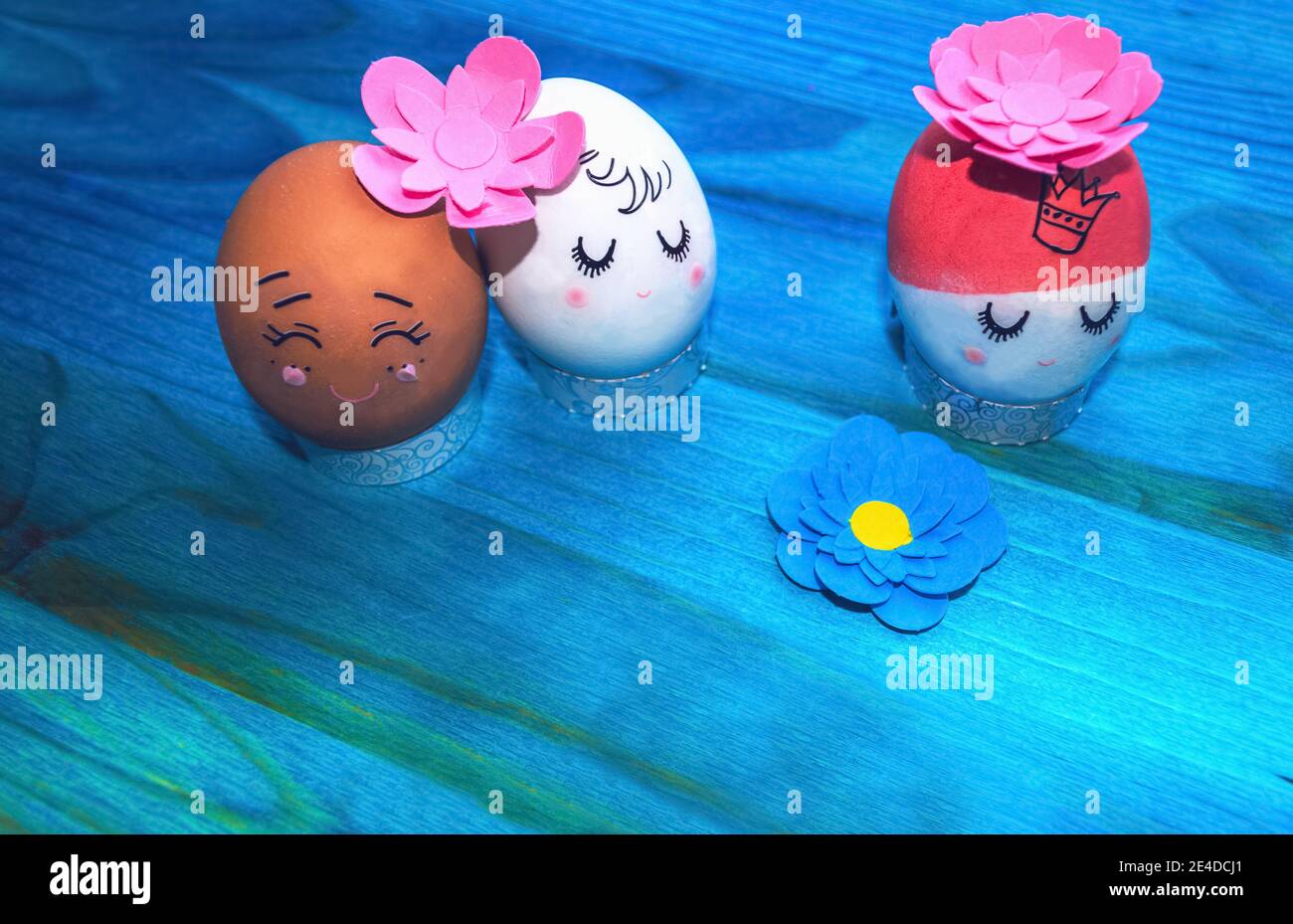 Famiglia e relazioni con uova di Pasqua e fiori di carta su sfondo di legno blu Foto Stock