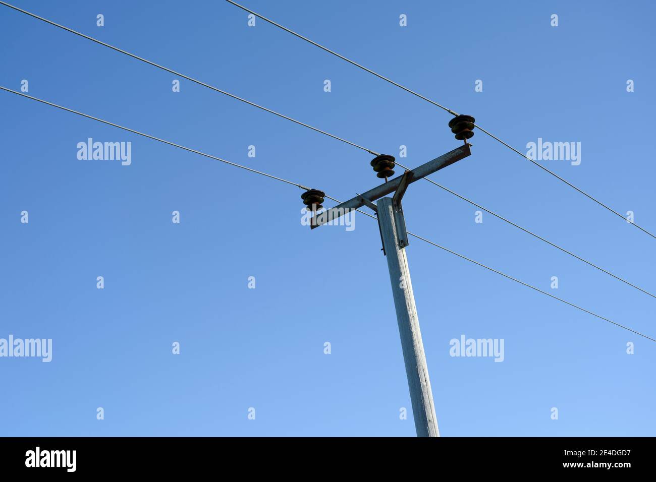 Cavi di alimentazione elettrica ad alta tensione e pilone di supporto contro un cielo blu luminoso Foto Stock