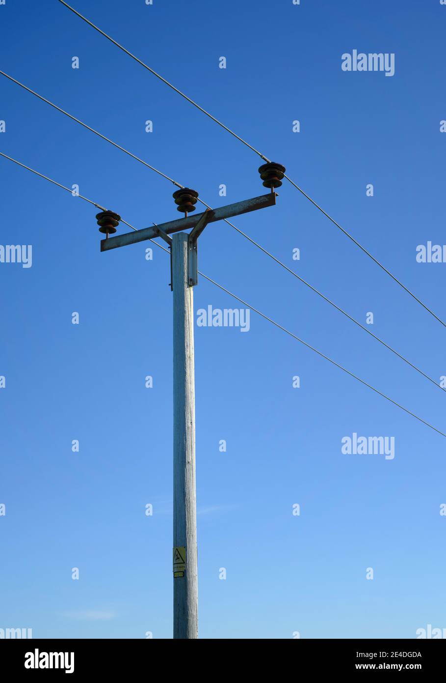 Cavi di alimentazione elettrica ad alta tensione e pilone di supporto contro un cielo blu luminoso Foto Stock